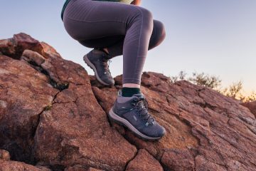 Women's legs, in grey leggings, descending a rock face with hiking boots on.
