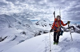 Caroline Gleich stands on top of a mountain with skis on her backpack.