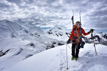 Caroline Gleich stands on top of a mountain with skis on her backpack.