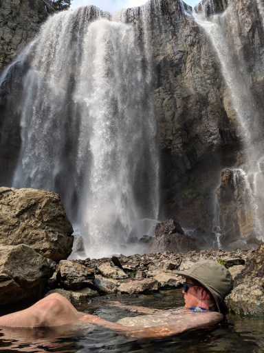 A backpacker lounges in a hot spring below Dunanda Falls in Yellowstone National Park.