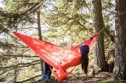 A person relaxes in a red hammock while reading.