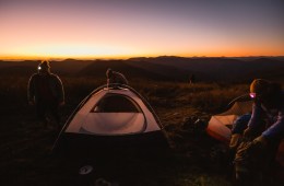 Three people setup camp as the sun sets.