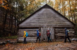 Hikers trudge by a wooden structure in Great Smoky Mountains National Park with the autumn leaves all around
