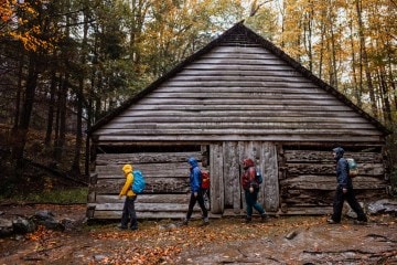 Hikers trudge by a wooden structure in Great Smoky Mountains National Park with the autumn leaves all around