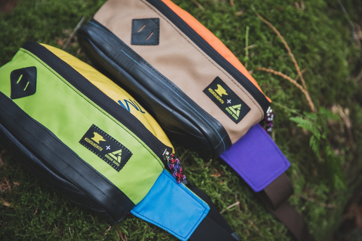 Two waistpacks of various colors lay on a mossy log.