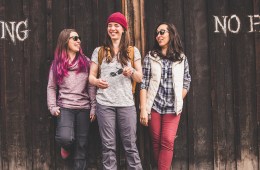 Three people leaning against a wall that says "no parking," laughing.