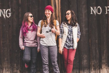 Three people leaning against a wall that says "no parking," laughing.