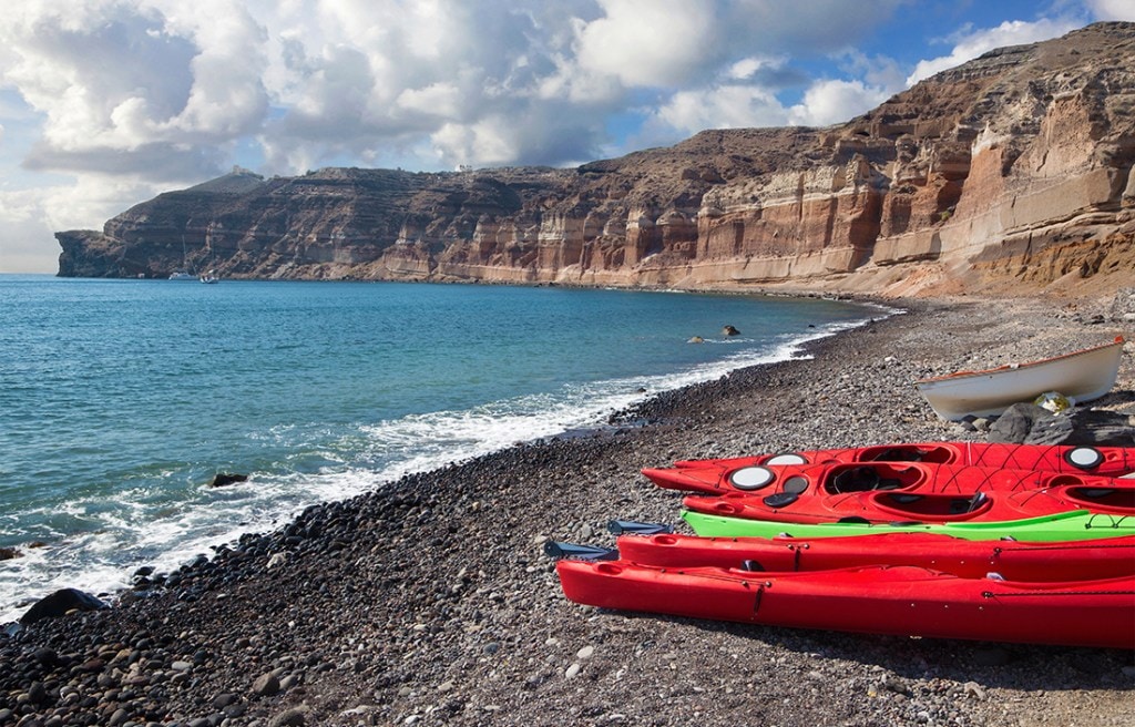 Kayaks sit at the ready in front of pristine beach cliffs. 