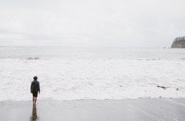 A person stands before a grey sky over a grey ocean.