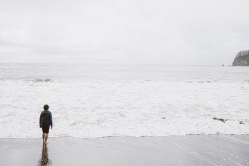 A person stands before a grey sky over a grey ocean.