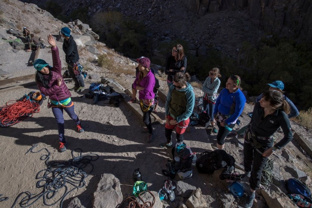 Olivia Hsu demonstrates body positioning for a climbing move while several other climbers look on.