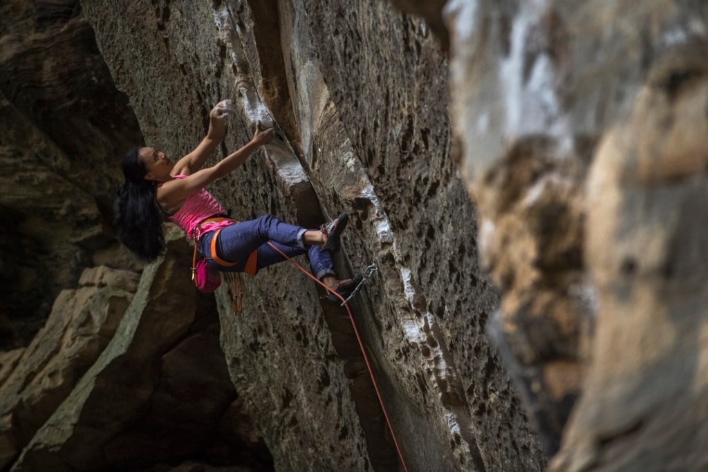 Rock climber and yogi Olivia Hsu reaches for a handhold on an overhanging climbing route.