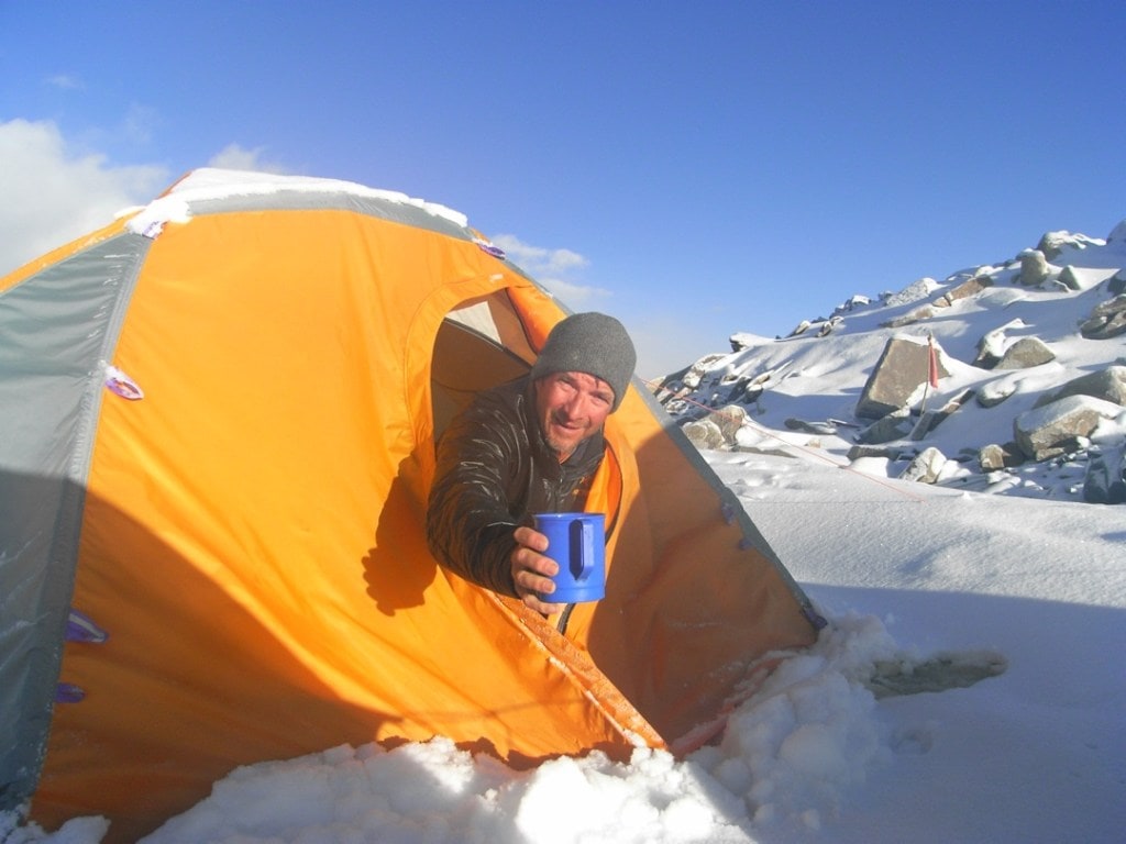 Steve Swenson reaches out of a yellow tent on Saser Kangri, an Indian peak, offering a mug. 