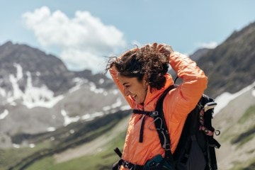 A hiker adjusts their hair against a backdrop of Colorado mountains