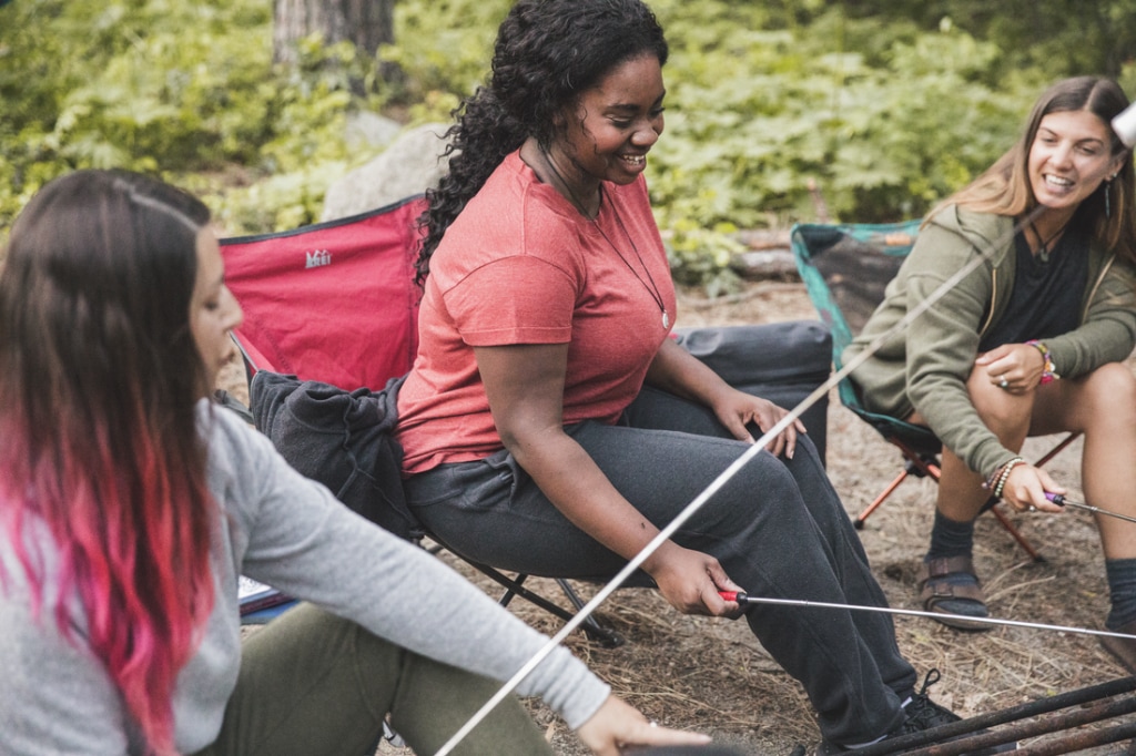 Three campers roast smores around a campfire.