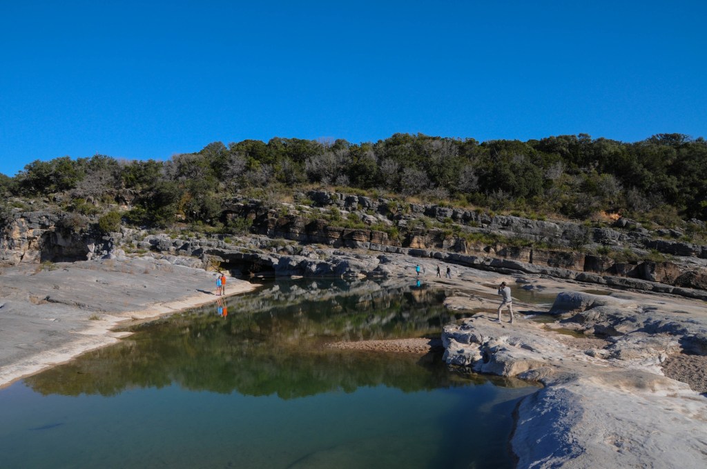 Several hikers walk along the rocks near Pedernales Falls.