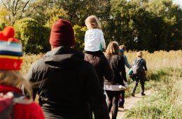 A child rides on her parent's shoulder during a hike.