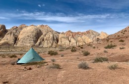 Tarp tent set up in the desert, short rocky mountains behind.