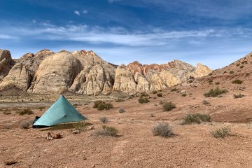 Tarp tent set up in the desert, short rocky mountains behind.