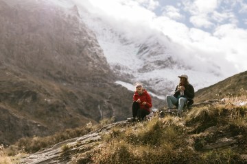 Two people sit on the ground, a huge snowy mountain is behind them.