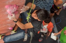Swee Mana reaches for a climbing hold on an arete while climbing on top rope in a gym.