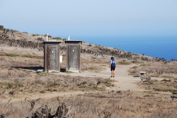 Person walks toward two outdoor toilets.