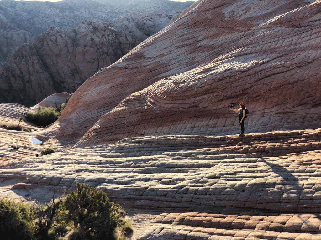 A woman snaps a photo in a beautiful desert setting with the sunlight pouring in