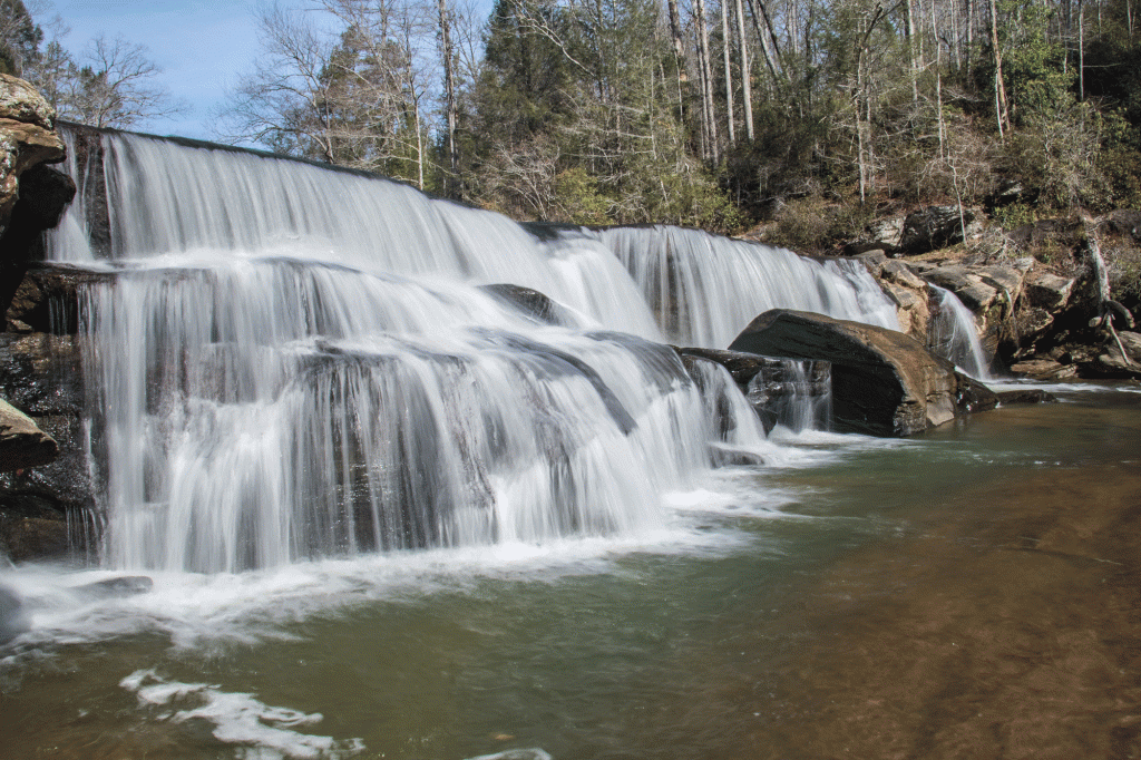 A wide waterfall rushes into a greenish-blue body of water