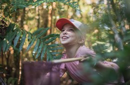 A woman peers through the forest with a smile on her face