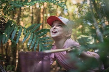 A woman peers through the forest with a smile on her face