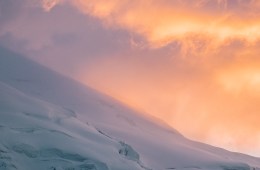Snowy, crevasse-riddled slope lit in the pinks and oranges of the sunset.