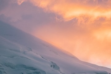 Snowy, crevasse-riddled slope lit in the pinks and oranges of the sunset.