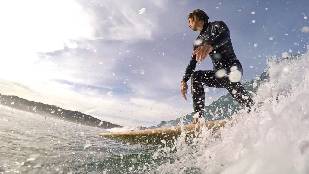 A surfer catches a wave under a cloudy ski