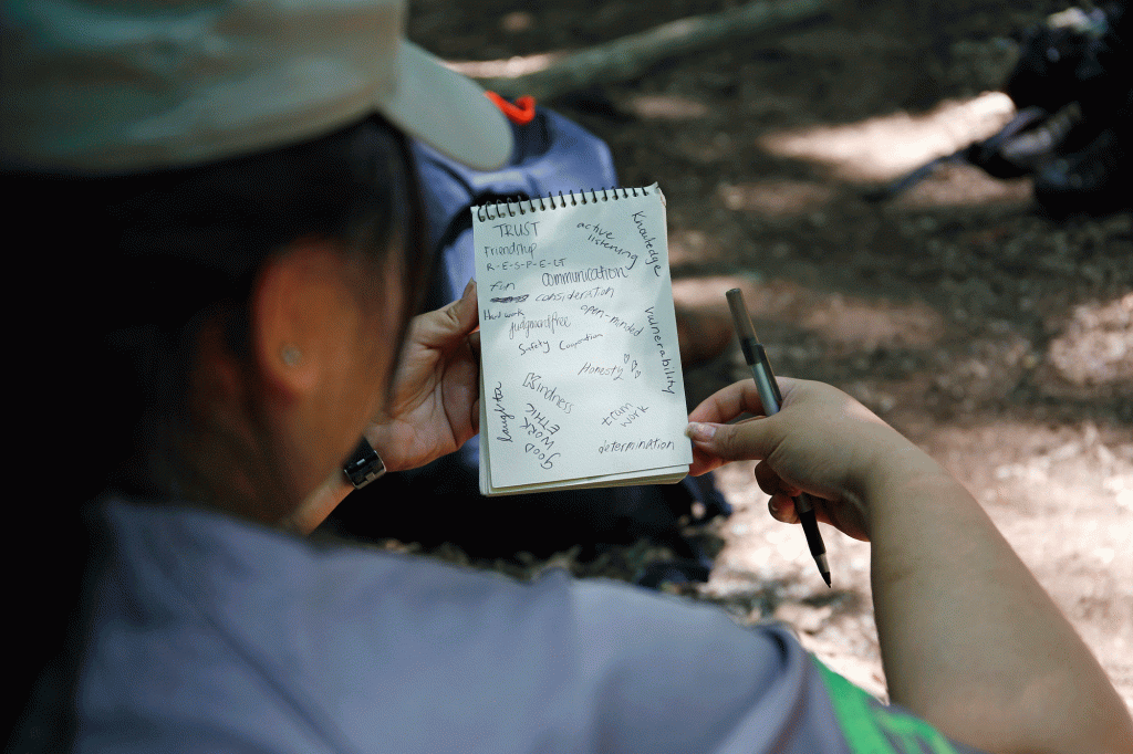 A woman records key words in a small spiral notebook on the trail