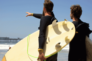 Two surfers stare out at a surf break under a blue sky