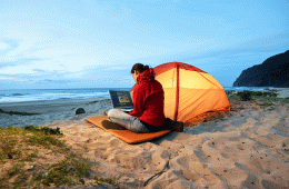 A woman working on a laptop beside her tent at dusk