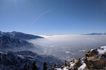 An overlook of valley cradled by mountains, covered with white, thin clouds.