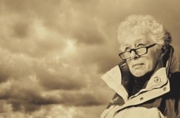 A woman wearing a sports jacket peers into the horizon with storm clouds behind her