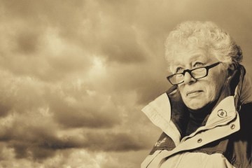 A woman wearing a sports jacket peers into the horizon with storm clouds behind her
