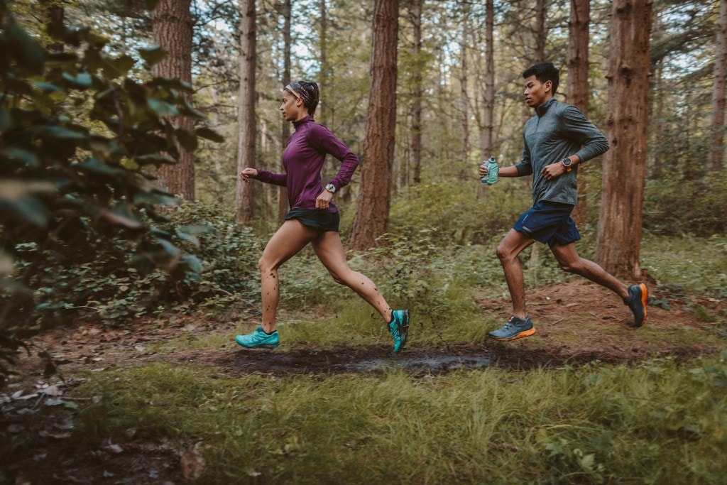 Two trail runners run together on a wooded trail.