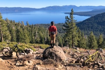 A person stands on a rock overlooking Lake Tahoe near a mountain bike trail