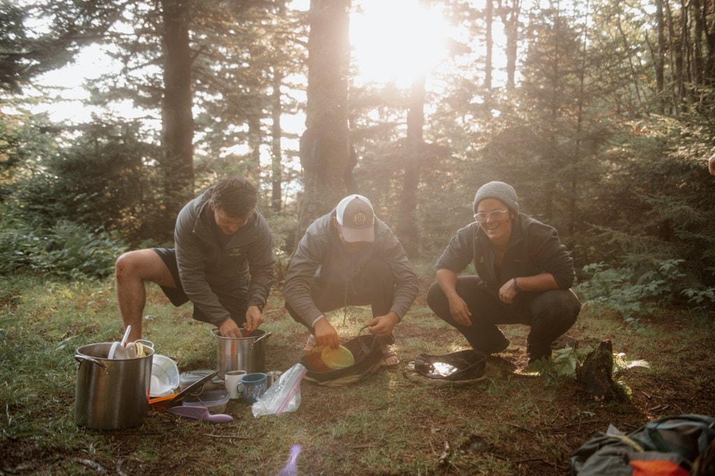 A SAWS crew cleans up after a meal with the sunlight filtering through the trees 