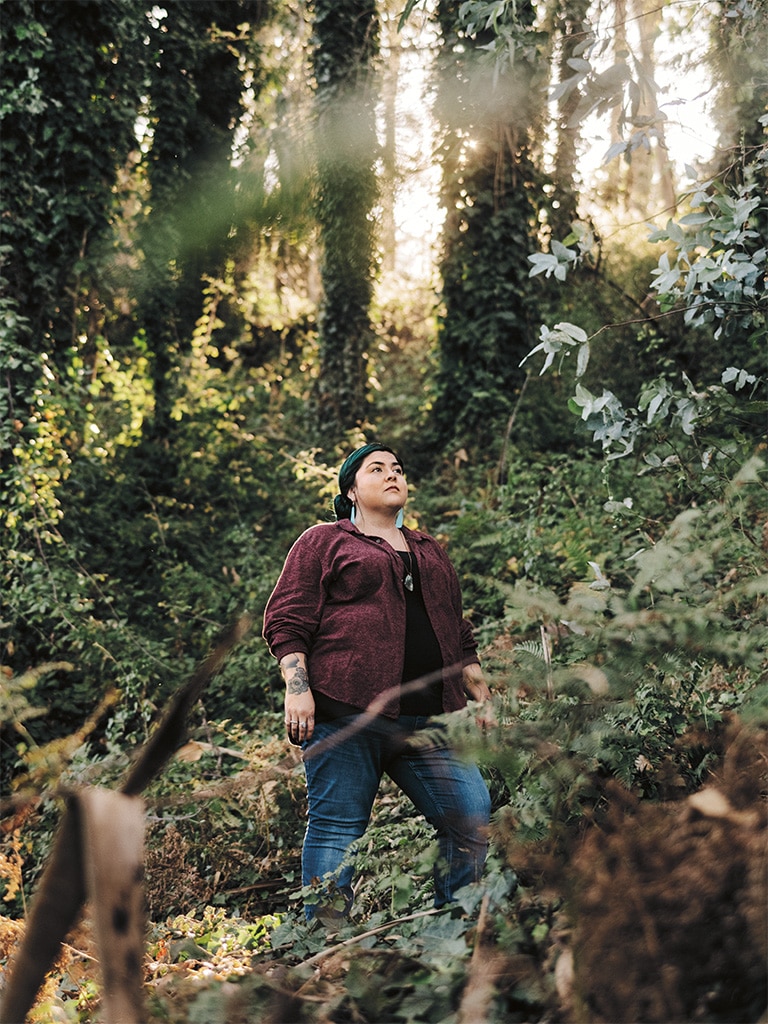 A woman stands proudly in a forest with sunlight streaming in