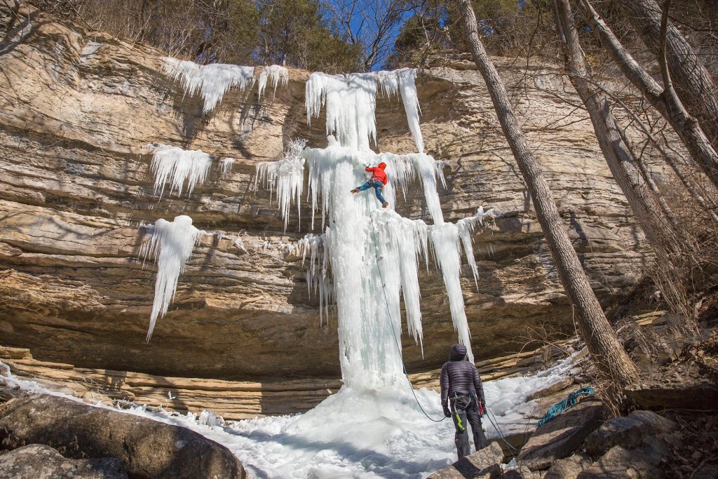 A climber in a red jacket sends a tall waterfall