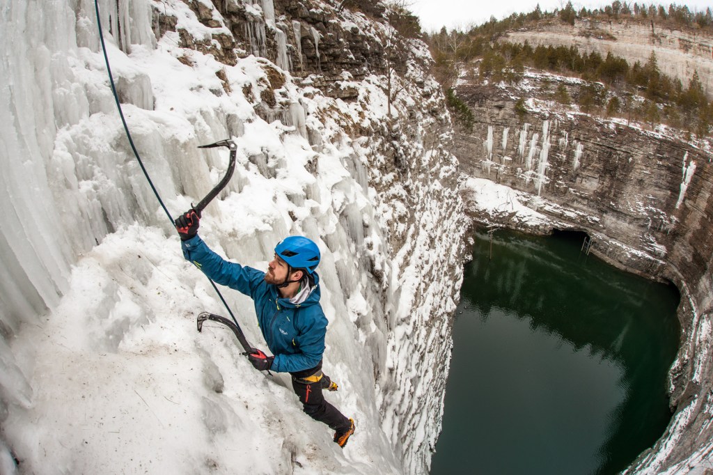 An up-close shot of a climber's face as he scales a column of ice above cold blue waters