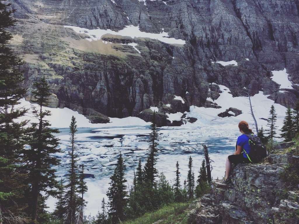 A hiker looks out over an ice filled Iceberg Lake.