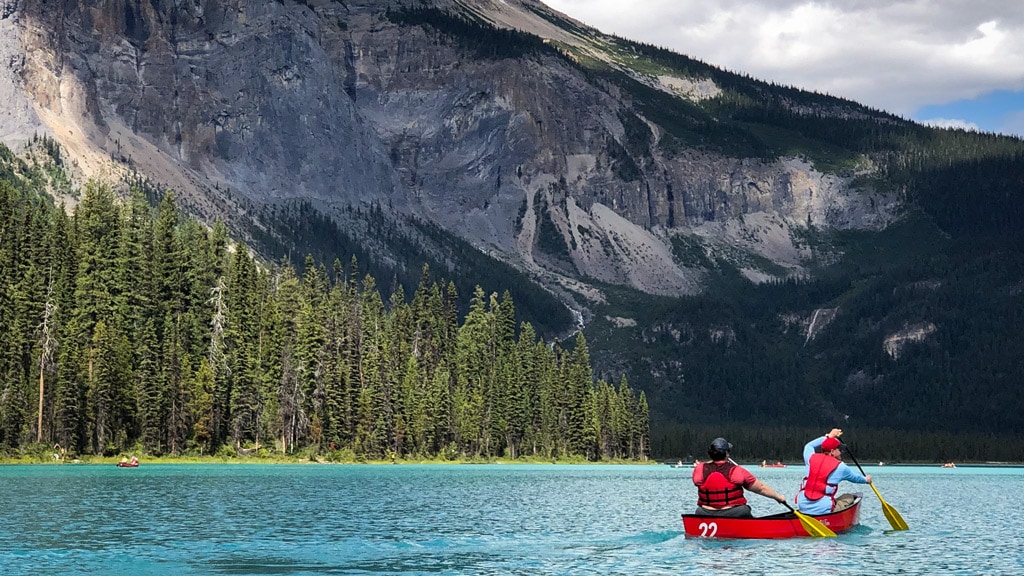 A person paddles a canoe on a lake with mountains in the background