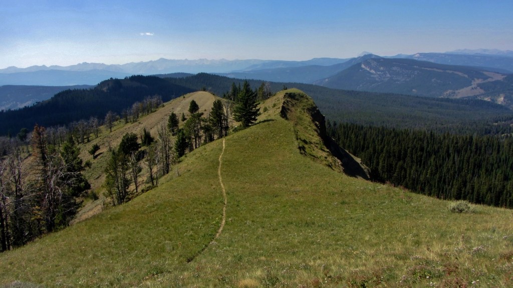 A thin trail snakes along a narrow, serpentine ridge, offering views of the surrounding mountains.