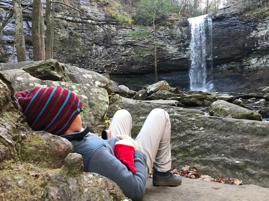 A child rests on a rock looking at a waterfall.