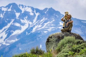 Ben Moon with his dog, Nori, sitting on a rock with a mountain range behind them.